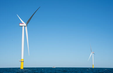 An offshore wind turbine. A boat sits in the background.