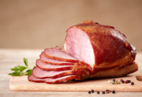 A ham on a cutting board. Half has been sliced. Photo by DepositPhotos