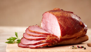 A ham on a cutting board. Half has been sliced. Photo by DepositPhotos