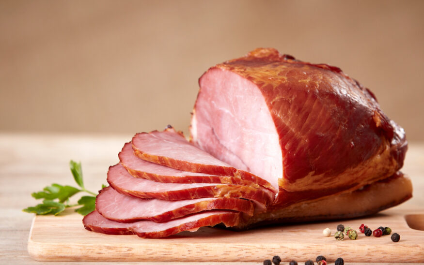 A ham on a cutting board. Half has been sliced. Photo by DepositPhotos