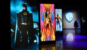 FILE - A visitor walks past portraits of DC Comics superheroes as she enters the "Action and Magic Made Here" interactive experience at the Warner Bros. Studio Tour Hollywood media preview on June 24, 2021, in Burbank, Calif. (AP Photo/Chris Pizzello, File)