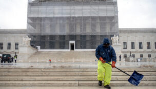 A worker shovels snow and ice in front of the Supreme Court building during the first snowfall of the winter season on Friday, Dec. 5, 2025, in Washington. (AP Photo/Mark Schiefelbein)