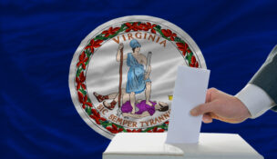 man putting ballot in a box during elections in front of flag american state of virginia