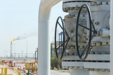 FILE PHOTO: A gas flare burns in the distance as valves and pipelines are seen at the Rumaila oil field in Basra
